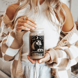 May include: A glass jar with a black and white illustration of an opossum with a pumpkin. The jar has a wooden lid and a straw. The text on the jar reads "19 THE OPOSSUM 51".