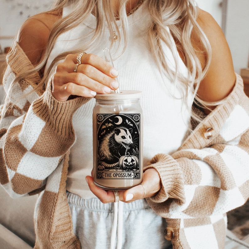 May include: A glass jar with a black and white illustration of an opossum with a pumpkin. The jar has a wooden lid and a straw. The text on the jar reads "19 THE OPOSSUM 51".