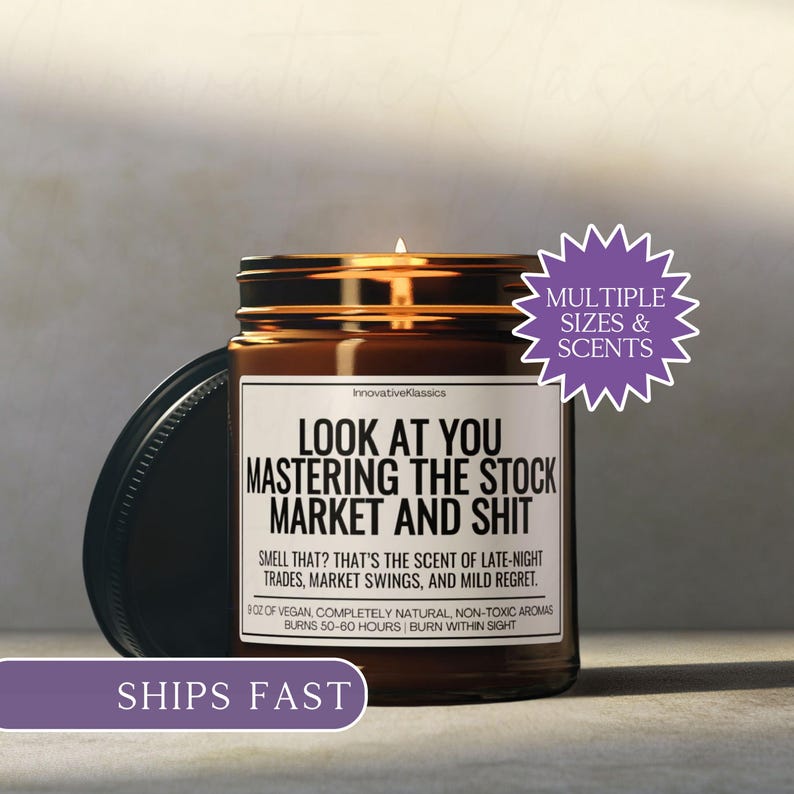 May include: A lit brown glass candle jar with a black lid. The label reads "LOOK AT YOU MASTERING THE STOCK MARKET AND SHIT." The candle is 9 oz and burns for 50-60 hours. The text "MULTIPLE SIZES & SCENTS" is also visible.