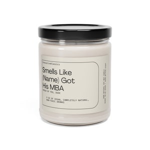 K&ouml;nnte beinhalten: Eine Glaskerze in einem Glas mit schwarzem Deckel. Das Etikett lautet "Smells Like (Name) Got His MBA. Proud of You, Dude. 9 oz of Vegan, Completely Natural, Non-Toxic Aromas."