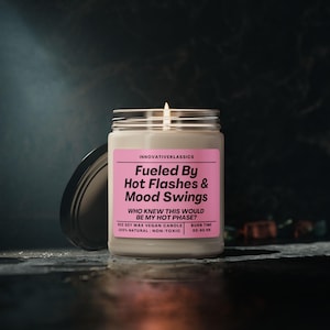 May include: A white candle with a pink label that reads "Fueled By Hot Flashes & Mood Swings" and "Who knew this would be my hot phase?" The candle is a soy wax vegan candle and is 100% natural and non-toxic. The candle has a burn time of 50-60 hours.