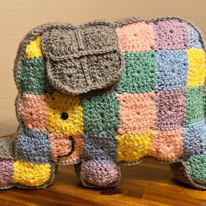 May include: A crocheted elephant toy with a patchwork design in shades of pink, blue, green, and yellow. The elephant has a gray crocheted trunk and ears.