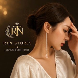 May include: A long silver-tone dangle earring featuring two thin chains encrusted with clear crystals, ending in a small crescent moon charm. A small crystal stud earring is worn in the upper ear cartilage. The text RTN STORES is visible.