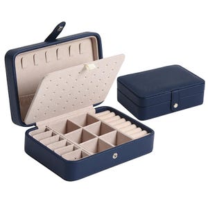 May include: A navy blue rectangular jewelry box with a snap closure. The interior is lined with beige fabric, featuring a hinged divider with earring holes, a ring roll section, and multiple square compartments for organizing small accessories.