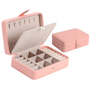 May include: A rectangular light pink jewelry box with a snap closure. The interior features a beige lining with a hinged divider, multiple square compartments for storage, and a section with padded slots for rings or earrings. One closed box is shown.