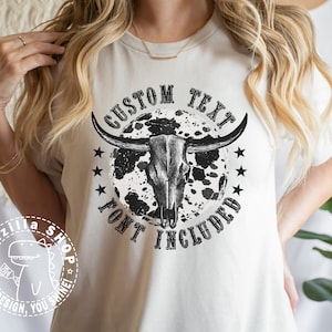 May include: A white t-shirt with a black and white graphic of a bull skull with a moon and stars. The text "CUSTOM TEXT FONT INCLUDED" is printed on the shirt.