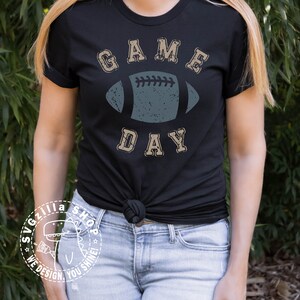 May include: A black t-shirt with a distressed, vintage-style graphic of a football and the text "GAME DAY".