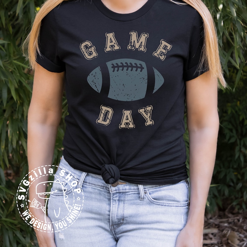 May include: A black t-shirt with a distressed, vintage-style graphic of a football and the text "GAME DAY".