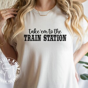 May include: White t-shirt with black text that reads "take 'em to the TRAIN STATION".