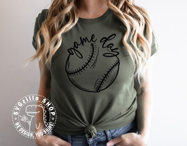 Op de afbeelding: Een groen T-shirt met de tekst "game day" en een zwart-witte baseball afbeelding.