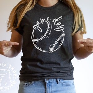 Op de afbeelding: Een donkergrijs T-shirt met een witte baseball en de tekst "game day" bedrukt op de voorkant.