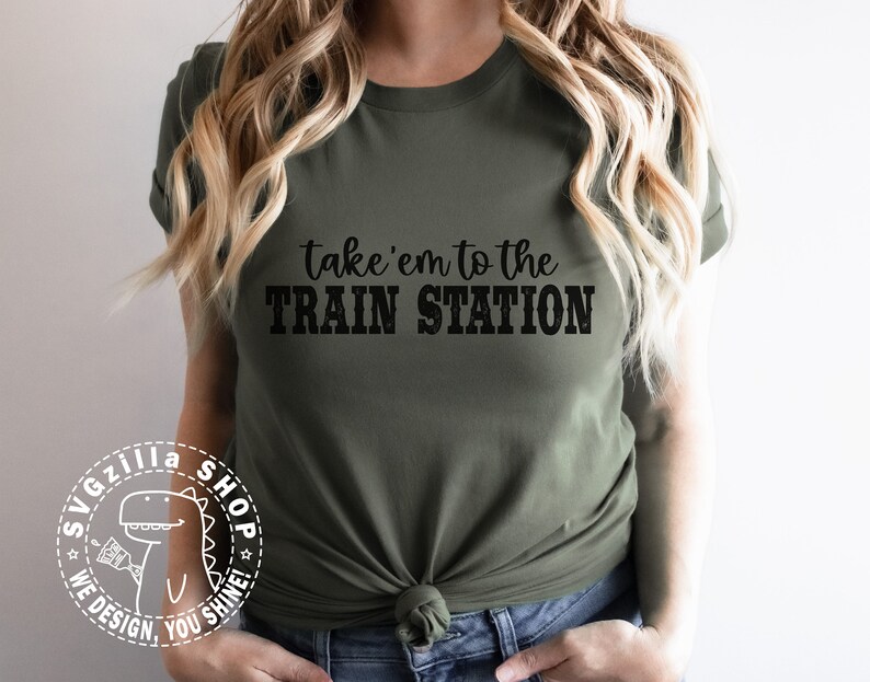 May include: A green t-shirt with the text "take'em to the TRAIN STATION" in black. The shirt has a white dinosaur logo with the text "SVGzilla SHOP WE DESIGN, YOU SHINE!"