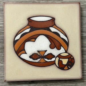 May include: Square ceramic tile with a Southwestern design. The tile features a brown and white pottery design with orange accents. A smaller, round design is next to the pottery. The tile has a beige background and a brown border.