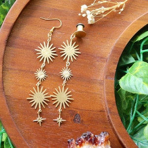 May include: Gold tone earrings with a dangling star design. The earrings feature multiple star shapes, including a larger star at the top and smaller stars cascading down.