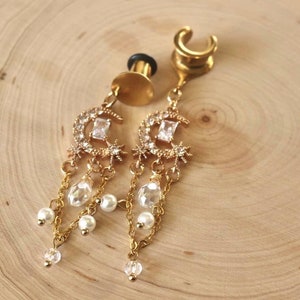 May include: A pair of gold-tone earrings with a crescent moon design, featuring clear crystals and dangling pearl and crystal beads.