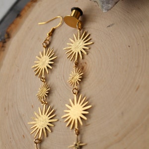 May include: A pair of gold-toned earrings with a dangling star design. Each earring features a series of five star-shaped charms, with the largest star at the top and the smallest star at the bottom.