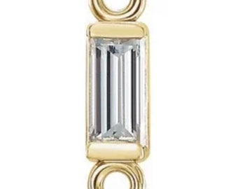 May include: Gold charm with a baguette-shaped diamond. The charm has two loops for attaching to a necklace or bracelet.