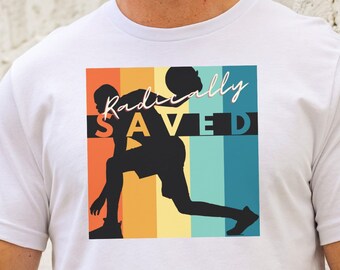 May include: White t-shirt with a retro-style graphic of a person playing basketball. The graphic has a rainbow color scheme and the text "Radically SAVED".