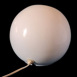 K&ouml;nnte beinhalten: Eine wei&szlig;e Globuslampe mit Kabel und Stecker. Die Lampe ist aus glattem, wei&szlig;em Material gefertigt und hat ein schlichtes, modernes Design.