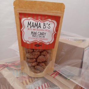 Könnte beinhalten: Ein klarer Beutel mit Mama B's Man Candy Maple Bacon. Der Beutel hat ein rot-weißes Etikett mit dem Text "Mama B's Nuts and Delicious Needs" und "ETSY@INEEDMAMABS". Der Beutel ist mit gezuckerten Nüssen gefüllt.