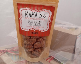 Puede incluir: Una bolsa transparente de Man Candy Maple Bacon de Mama B's. La bolsa tiene una etiqueta roja y blanca con el texto "Mama B's Nuts and Delicious Needs" y "ETSY@INEEDMAMABS". La bolsa está llena de nueces azucaradas.