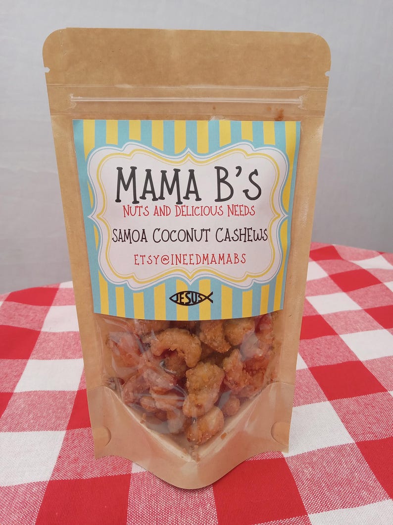 May include: A clear plastic-windowed bag of Samoa Coconut Cashews. The bag is brown with a colorful label that reads "Mama B's Nuts and Delicious Needs". The label has a blue and yellow striped background and the text "Samoa Coconut Cashews".
