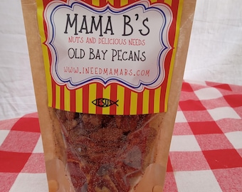 Puede incluir: Una bolsa de papel marrón con una etiqueta a rayas rojas y amarillas que dice "Mama B's Nuts and Delicious Needs Old Bay Pecans www.ineedmamab's.com". La bolsa está llena de nueces de pecán.
