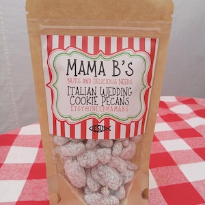 May include: A clear plastic bag filled with Italian Wedding Cookie Pecans. The bag has a label with the text "Mama B's" and "Nuts and Delicious Needs". The label has a red and white striped design. The bag is on a red and white checkered tablecloth.