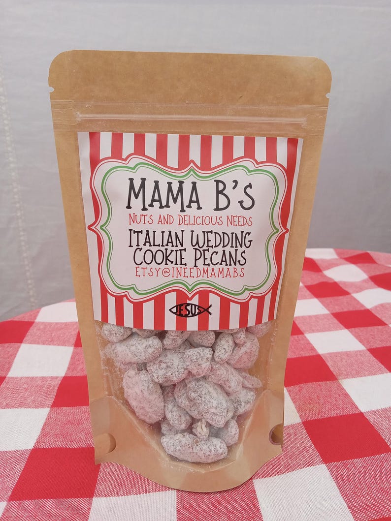 May include: A clear plastic bag filled with Italian Wedding Cookie Pecans. The bag has a label with the text "Mama B's" and "Nuts and Delicious Needs". The label has a red and white striped design. The bag is on a red and white checkered tablecloth.