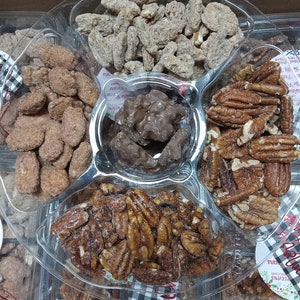 May include: A clear plastic tray filled with various candied nuts and chocolate clusters. The tray is divided into sections containing sugared pecans, almonds, and other nut varieties. The nuts are coated in a light brown sugar glaze.