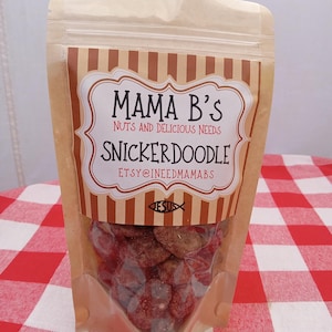 May include: A clear plastic bag filled with Snickerdoodle candies. The bag has a brown and white striped label that reads "Mama B's Nuts and Delicious Needs Snickerdoodle" with the Etsy shop name. The candies are red and brown.