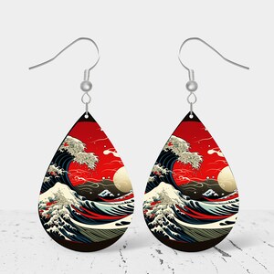 May include: A pair of teardrop-shaped earrings with a red, white, and blue image of a large wave crashing against a red background. The earrings are silver and have a hook closure.