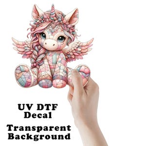 May include: A colorful unicorn decal with a transparent background. The unicorn is depicted in a seated position with wings, a horn, and a floral crown. The text "UV DTF Decal" and "Transparent Background" are visible.