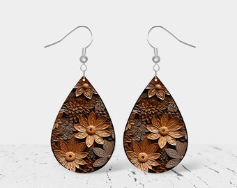 Puede incluir: Un par de pendientes en forma de lágrima con un diseño floral. Los pendientes están hechos de metal marrón y dorado y tienen un gancho plateado.