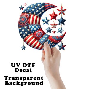 May include: A crescent moon decal featuring a patchwork design of red, white, and blue patterns, including stars and stripes. Several star-shaped ornaments in matching colors hang from the moon. The text UV DTF Decal Transparent Background is visible.