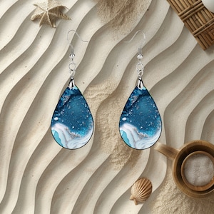 May include: A pair of teardrop-shaped earrings with a blue and white abstract design. The earrings are made of resin and have silver hooks.