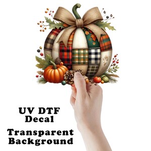 May include: A decorative pumpkin decal with a patchwork design in various plaid patterns. The pumpkin is adorned with a burlap bow, surrounded by fall foliage, a small orange pumpkin, and pinecones. The text "UV DTF Decal Transparent Background" is at the bottom.