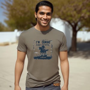 May include: A brown t-shirt with a graphic print of a cowboy riding a horse. The text on the shirt reads "I'm Coming & Hell's Coming with me".