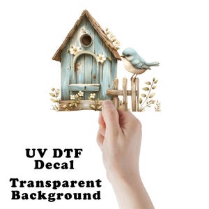 May include: A blue bird perches on a wooden fence next to a blue birdhouse with a white picket fence. The birdhouse has a white roof and white flowers around the opening. The background is transparent.