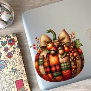 May include: A decorative pumpkin sticker with a plaid design, a brown bow, and autumnal accents like berries and acorns. The sticker is on a silver laptop.
