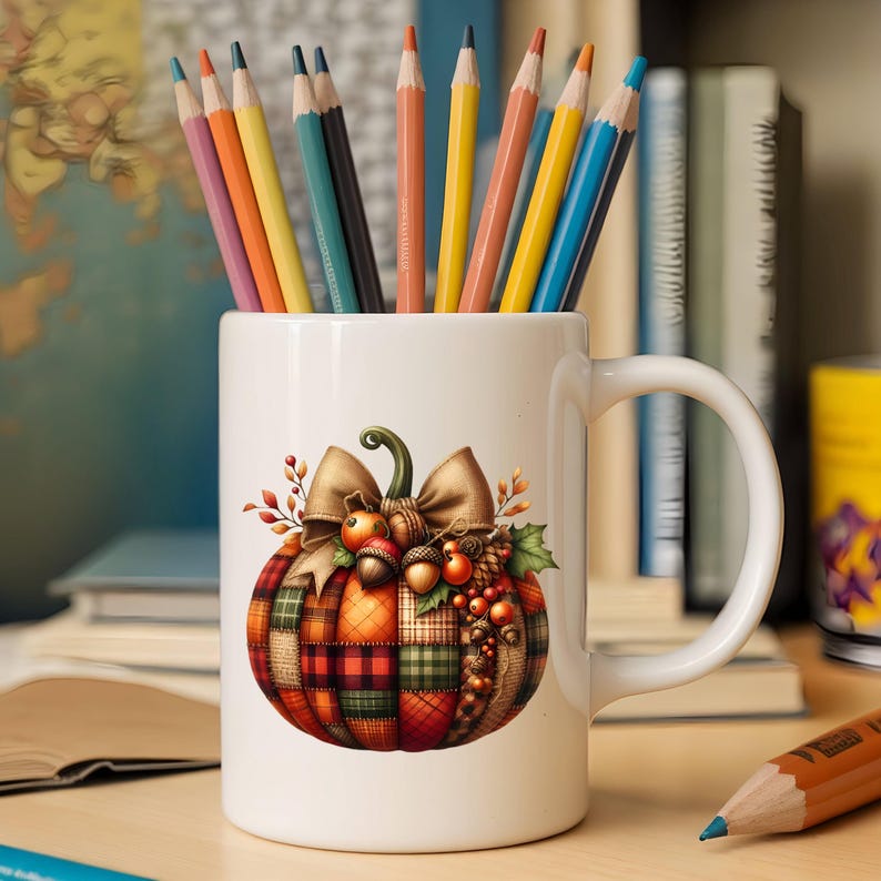 May include: White ceramic mug with a handle, featuring a colorful patchwork pumpkin with a brown bow and acorns. The mug is filled with colored pencils.