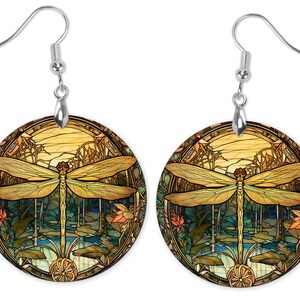 May include: A pair of round, gold and green stained glass earrings featuring a dragonfly in a forest scene.