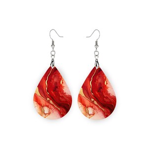 May include: A pair of teardrop earrings with a red, gold, and white abstract design. The earrings hang from silver-colored fish hook ear wires. The earrings have a marbled effect, with the colors blending together.