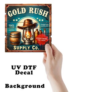 May include: A rectangular decal featuring a wood-plank design with the text GOLD RUSH SUPPLY CO. The graphic includes a brown cowboy hat, a lit lantern, a wooden barrel, and metal bottles. A red paint splatter contains the text EVERYTHING YOU NEED.