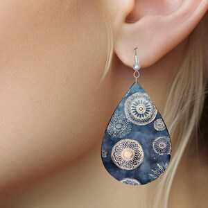 Pu&ograve; includere: Un paio di orecchini a forma di goccia con sfondo blu scuro e un motivo a mandala bianco.