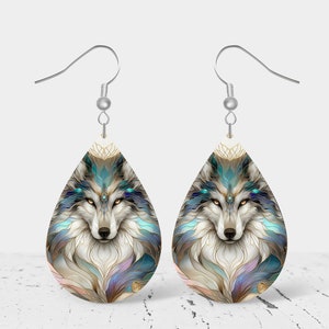 May include: A pair of silver teardrop-shaped earrings with a wolf face design. The wolf has blue eyes and is surrounded by a colorful, abstract pattern.