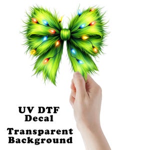 May include: A green bow with colorful Christmas lights, a UV DTF decal with a transparent background. The bow is held by a hand. The text "UV DTF Decal" and "Transparent Background" is visible.