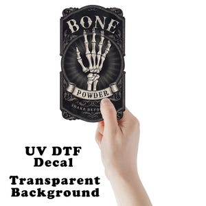 May include: A black and white decal with the words "BONE POWDER" and a skeleton hand illustration. The decal has a transparent background and the text "UV DTF Decal" is printed below.