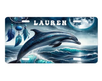 May include: A license plate depicting a dolphin leaping from ocean waves under a full moon. The dolphin is blue with detailed patterns. The name "LAUREN" is in white letters above the dolphin. A dreamcatcher and feathers are on the left.