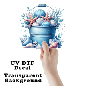 May include: A blue metal bucket filled with seashells and starfish. The bucket is surrounded by green leaves and white flowers. The text "UV DTF Decal Transparent Background" is written below the bucket.